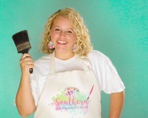 Tamara holding a paint brush and wearing a painting apron