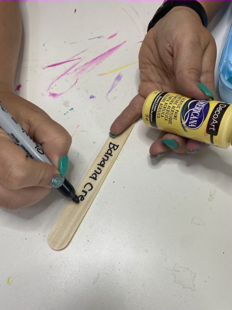 Tamara writing "banana cream" on a craft stick with a Sharpie and yellow paint