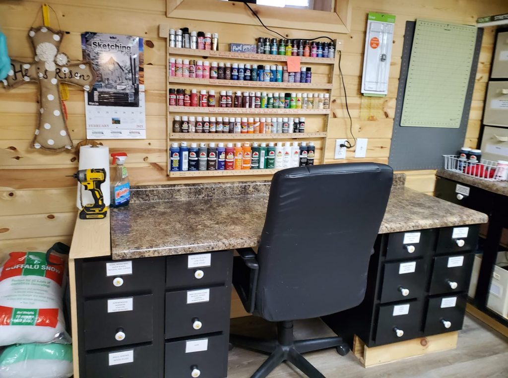 desk and chair with wooden shelves of paint bottles above