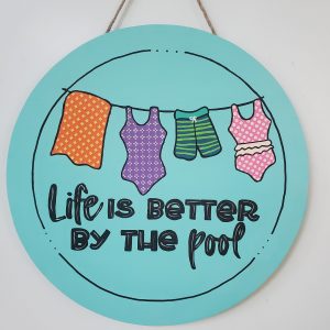 Baby Blue round door hanger that reads "life is better by the pool" with swimsuits on it