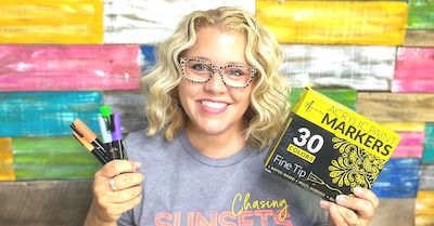 Tamara holding paint pens and a box of Artistro paint pens