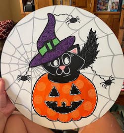 witch cat sitting in a jack o lantern on a spider web background of a door hanger