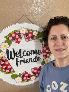 woman with door hanger that has flowers and says "welcome friends"