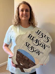 woman holding a Christmas door hanger that says "Jesus is the reason for the season"