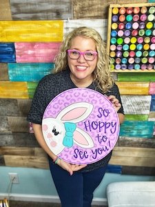 Tamara holding a "hoppy to see you" door hanger with a bunny on it