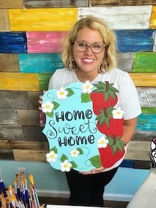 Tamara holding a door hanger with strawberries that say "Home sweet home"