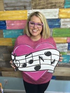 Tamara holding a school door hanger that is a heart with musical notes on it