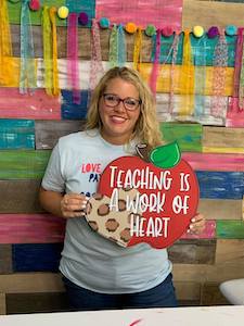 Tamara holding an apple door hanger that says "teaching is a work of heart"